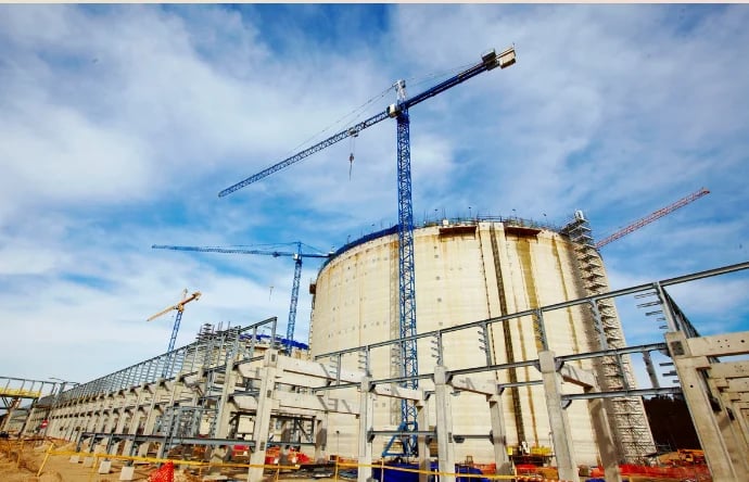 Industrial construction site with large concrete storage tank and multiple construction cranes against blue sky