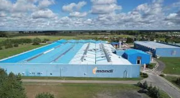 Aerial view of a large blue indoor swimming facility with multiple lanes, branded with Mondi logo, surrounded by green landscape